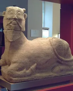 Bicha of Balazote sculpture with a human head and bovine body reclining on the ground.