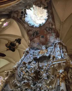 The Transparente in Toledo Cathedral, showing a richly carved Baroque altarpiece beneath a circular ceiling opening with painted celestial scenes.