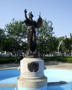 Russell Alger Memorial Fountain with a bronze female statue holding a shield and sword in a blue basin.