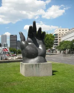 Dark Botero hand sculpture with curled fingers on a concrete plinth.