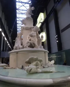 Fons Americanus by Kara Walker, a large white tiered fountain with sculpted figures and sea creatures inside a vast industrial hall.