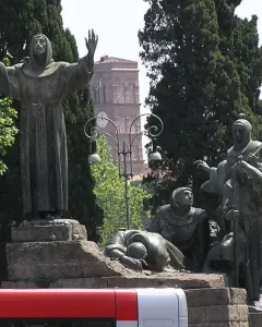 Bronze Monument to Saint Francis of Assisi with robed figures on a stepped stone plinth under a blue sky.