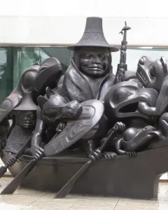 Spirit of Haida Gwaii sculpture showing a dark canoe filled with human and animal figures in a shallow pool