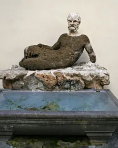 Babuino Fountain with a reclining stone figure over a rectangular basin of greenish water.