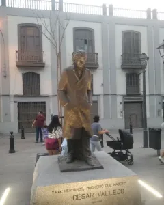 Bronze statue of César Vallejo on a stone pedestal in a paved square.