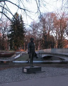 Pushkin statue on a dark pedestal in a park with bare trees and a bridge in the background