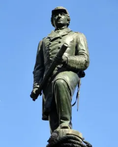 Admiral David G. Farragut statue in bronze with a green patina, holding a telescope against a blue sky.