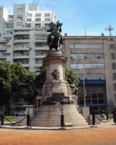 Bronze equestrian monument to Giuseppe Garibaldi on a tall stone pedestal in a city plaza, with trees and surrounding buildings.