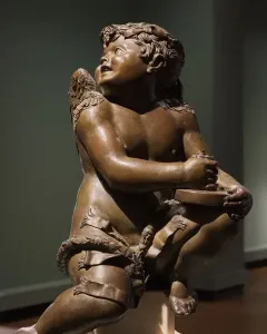 Bronze candelabra angel sculpture with wings, a wreath, and a garland, looking upward while holding a circular object.