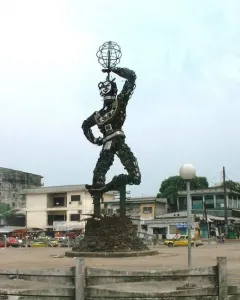 La Nouvelle Liberté sculpture rising on a stone base in an urban square, with one arm raised holding a spherical metal form.