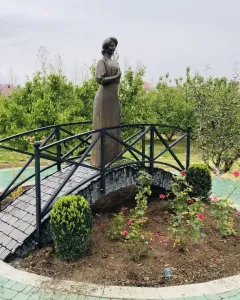 Bronze statue of Zabel Yessayan holding a book on a small arched bridge in a circular garden bed.