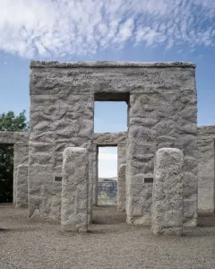 Maryhill Stonehenge with rough gray stone pillars and lintels framing a view of dry rolling hills under a blue sky.