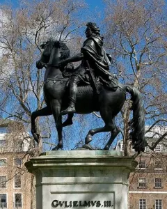 William III equestrian statue on a stone pedestal in St James\'s Square, with bare branches and buildings behind it.