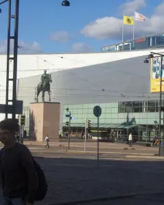 Marshal Mannerheim equestrian statue in front of a modern glass building in Helsinki, with a pedestrian in the foreground.