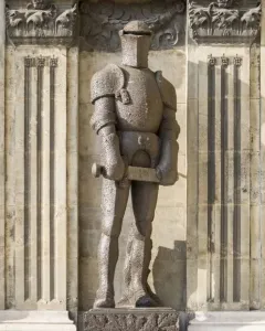 Wehrmann in Eisen, a dark armored knight statue with a hammer, standing on a carved pedestal against a stone facade.