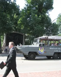 The Shaw Memorial appears behind trees and a stone wall, with a Boston Duck Tours vehicle passing in front.