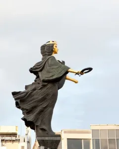 Statue of Sofia, a monumental female figure with a gilded face and crown, holding a wreath on a tall pedestal.