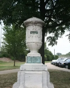 The Cuban Friendship Urn on a tiered stone pedestal with a bronze plaque, standing in a grassy park near a path and trees.
