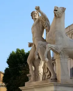 White marble Horse Tamers sculpture with a muscular figure beside a rearing horse on a stone pedestal.