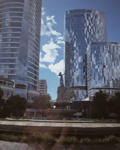 Diana the Huntress Fountain with a figure drawing a bow against a clear sky and city skyscrapers.