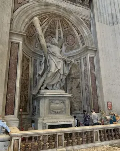 Saint Andrew sculpture standing in an ornate alcove inside St. Peter\'s Basilica, with a carved pedestal and visitors below.