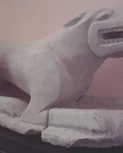 Leona de Baena stone lioness sculpture on a dark base against a pale wall.
