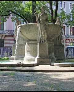 Nornenbrunnen stone fountain with three draped female figures and cascading water in Munich.
