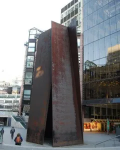 Fulcrum, a large rusty metal sculpture with leaning panels forming a triangular opening in an urban plaza.