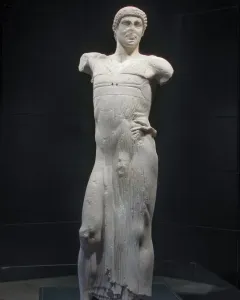 The Motya Charioteer, a white marble male statue missing its arms, shown against a dark background.