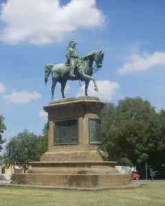 Victor Emmanuel II Monument shown as a dark bronze equestrian statue on a stone pedestal with grass and trees behind it.