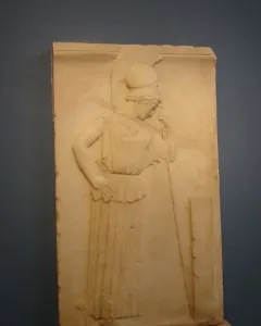 Mourning Athena relief showing a helmeted female figure in profile, leaning on a staff beside a rectangular stele.