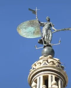 The Giraldillo sculpture of a robed woman holding a shield and palm frond against a blue sky.