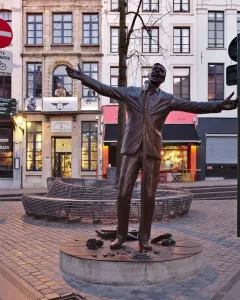 L\'Envol bronze sculpture of a man in a suit singing into a microphone with his arms outstretched in a cobblestone square.