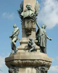 Upper section of the Rius i Taulet Monument with a bronze bust on an obelisk, flanked by bronze figures and a small putto holding a branch.
