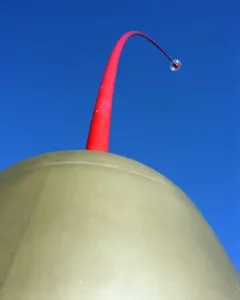 Wind Wand sculpture with a crimson rod rising from a rounded dome against a blue sky.