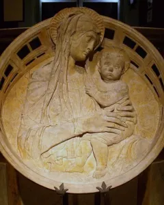 Madonna del Perdono relief showing a haloed mother holding a child, with cherubs in the background and a decorative border.