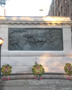 Firemen\'s Memorial with a stone relief of horses pulling a wagon, flanked by statues and wreaths.