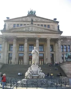 Schiller Monument with seated allegorical figures at its base in front of a classical building.