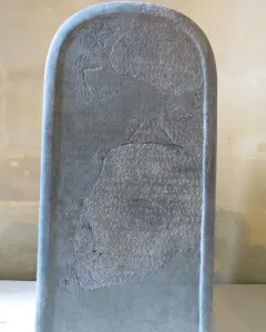 Mesha Stele, a tall dark stone slab covered in ancient carved script with missing fragments and visible cracks.