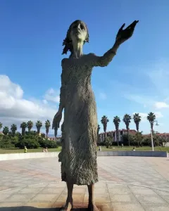 La madre del emigrante bronze statue of a woman standing barefoot with one arm outstretched in a plaza