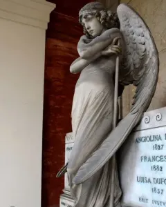 Monteverde Angel, a winged stone angel with bowed head and crossed arms holding a long staff, standing on a tiered base.