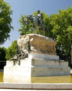 Monument to General Martínez-Campos with an equestrian bronze statue on a tiered stone pedestal in a pool surrounded by trees.