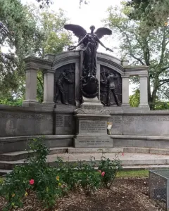 Titanic Engineers\' Memorial with a winged female figure above bronze relief panels in a park setting.