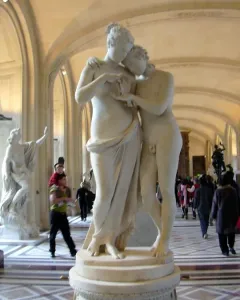 Standing Psyche and Love marble sculpture displayed on a pedestal in a museum gallery with visitors in the background.
