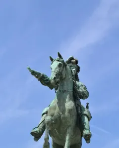 Equestrian Statue of Louis XIV, a green-patinated bronze rider on a rearing horse pointing forward against a blue sky.