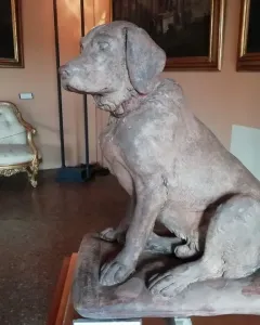 Cane Tago, a seated terracotta dog sculpture with a faint red collar.