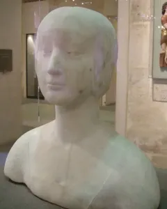 White marble bust of a princess with a serene expression and close-fitting cap on a dark base in a museum display.