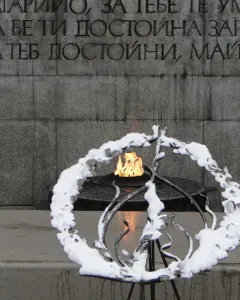 The Unknown Soldier Monument with a grey stone wall, Cyrillic inscription, and an eternal flame in a dark metal basin.