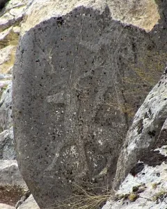 Karasu relief carved on a weathered dark stone slab among larger rocks.