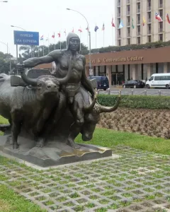 La yunta bronze sculpture of a man guiding two oxen on a lawn beside a patterned walkway.